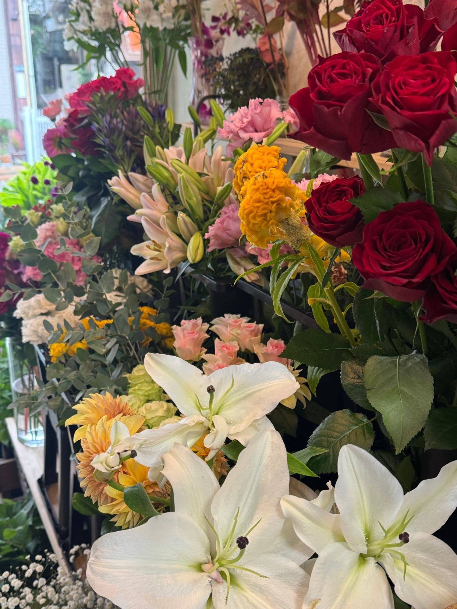 店頭に並ぶ赤いバラ・ユリ・ケイトウなどのお花